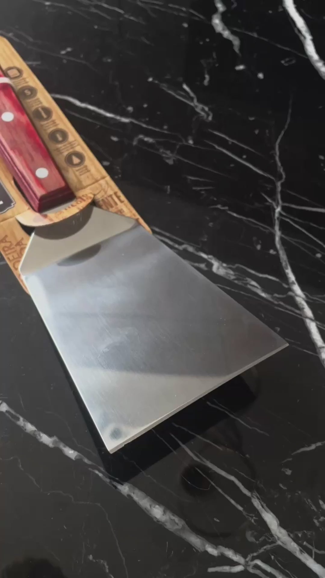 Vídeo de anúncio da espátula de fritura Tramontina, com lâmina de inox de 5 polegadas e cabo em madeira Polywood vermelho. Ideal para uso em chapas, a espátula garante praticidade e durabilidade. Encontre essa ferramenta essencial para lanches e preparos rápidos.